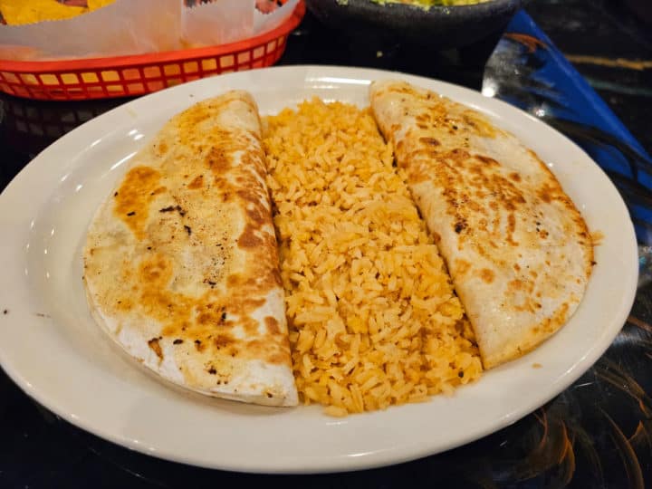 two cheese quesadillas with rice on a white plate next to a basket of chips. 