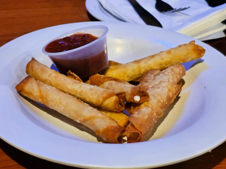 Cheese sticks on a white plate with a plastic cup of marinara 