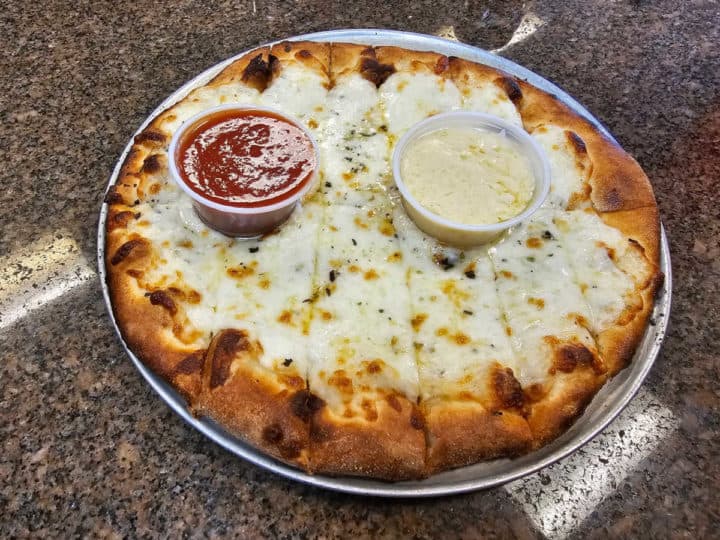 cheesy bread on a silver platter with ramekins of tomato sauce and garlic cream sauce. 