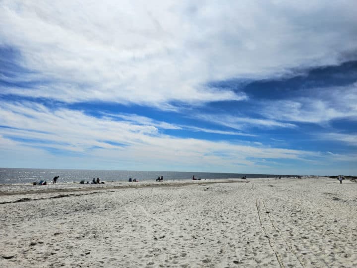 large beach with people in the distance, blue skies and some clouds