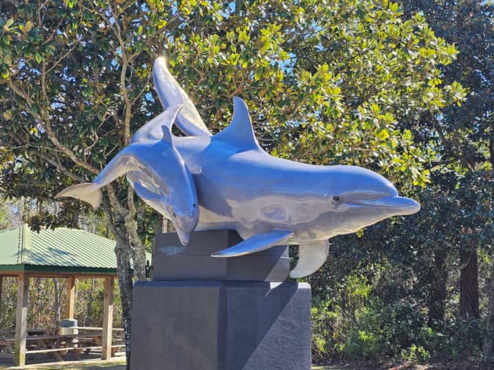 Dolphin and baby statue on a pedestal with trees in the background. 