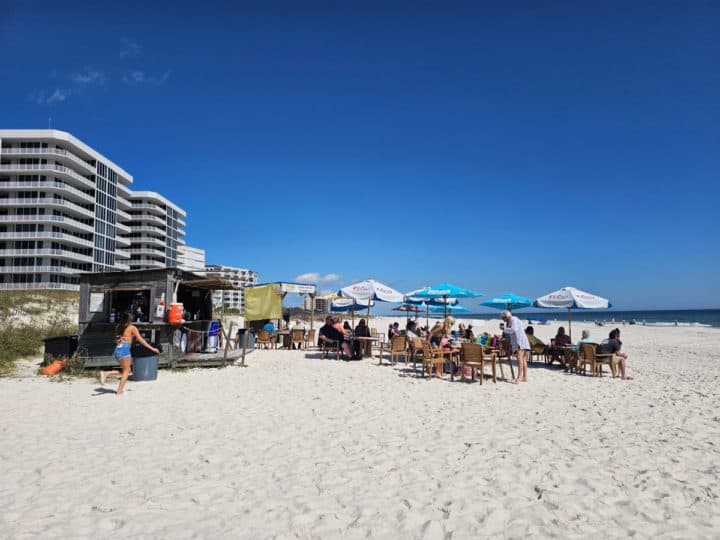 Flora Bama Beach Bar on the white sand with a music stage, tables and chairs looking out at the Gulf of Mexico
