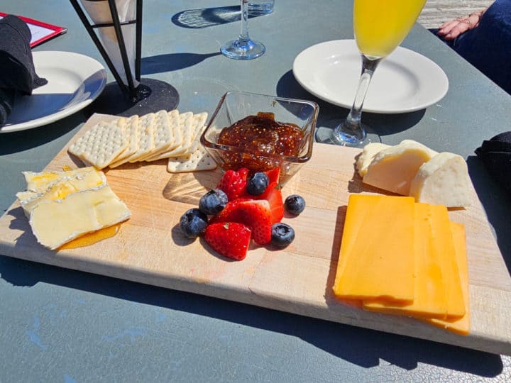 Cheese and fruit platter on a wooden board next to a mimosa
