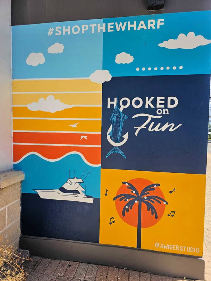 Painted mural with Hooked on Fun, a boat, #shopthewharf, and palm trees