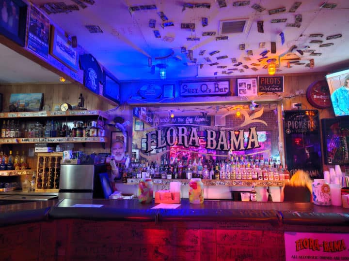 indoor bar with Flora Bama printed on the mirror, dollar bills on the ceiling and glasses on the bar