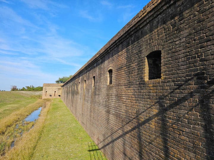 Looking down the brick wall of Fort Gaines with grass blow and some water in a moat. 