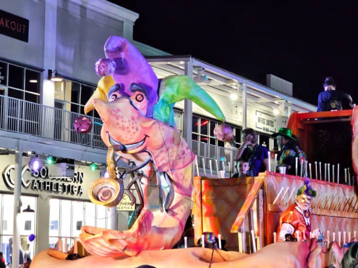 Mardi gras float with shrimp wearing a jesters hat and people dressed up on Main Street in the Wharf