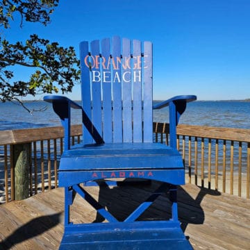 Large Orange Beach Adirondack Chair on a wooden dock with water in the background