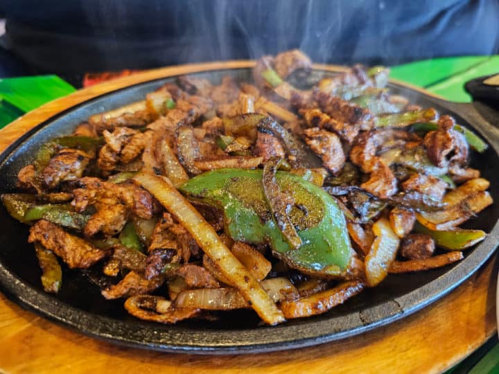 Steak fajitas sizzling on a cast iron skillet on the table 