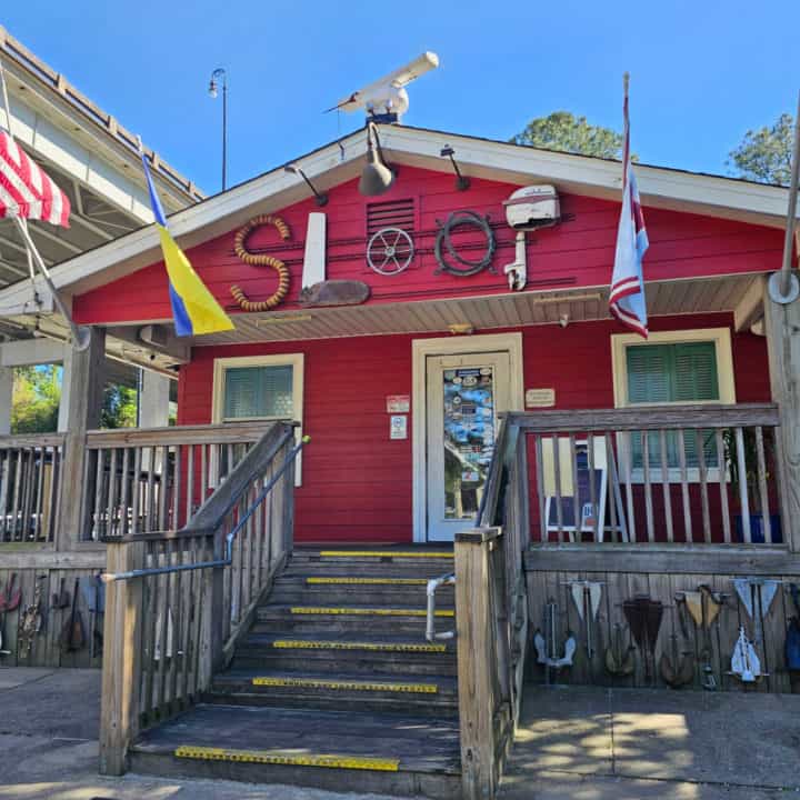 Sloop written with boat parts on a red building with flags and stairs leading to the front entrance. 
