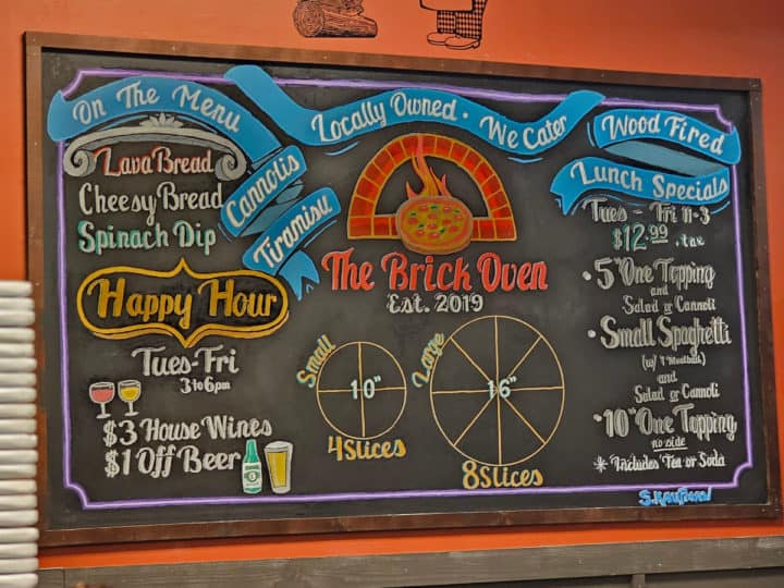 Chalkboard with The Brick Oven logo, lunch specials, happy hour, and pizza sizes 