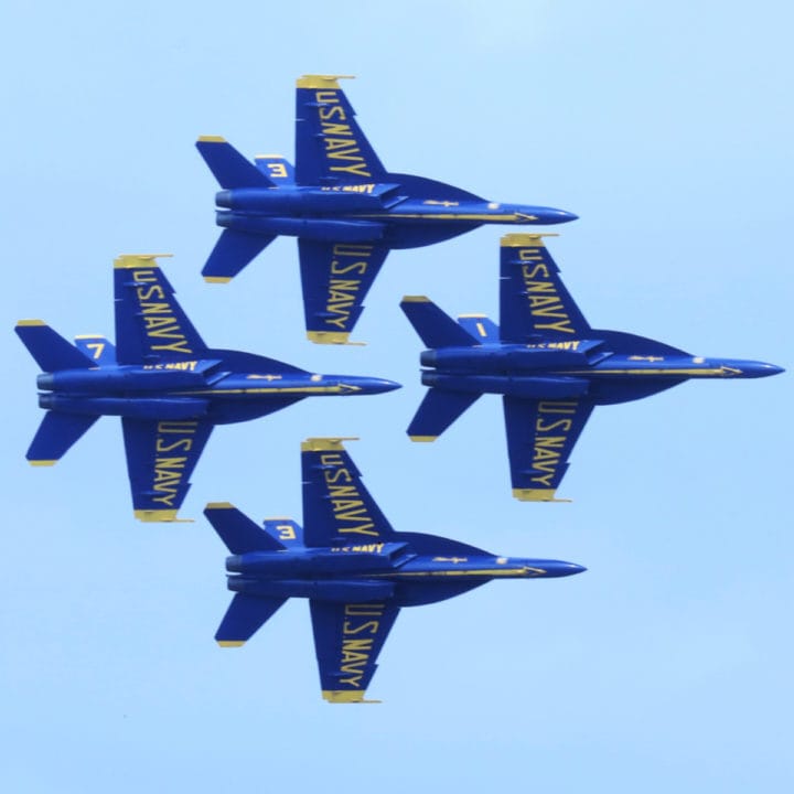 Four Blue Angels planes in a diamond pattern with blue sky