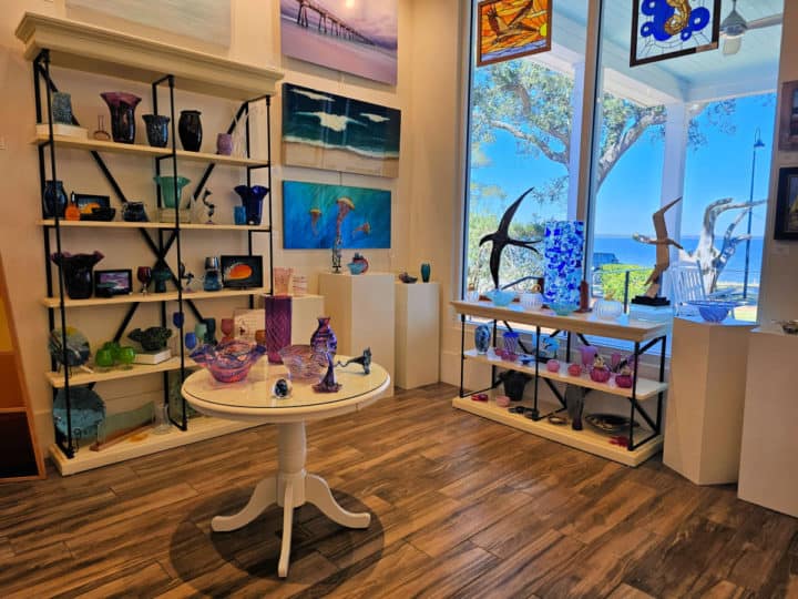 Shelves of blown glass art plus photos on the gallery wall. Window looking out to the water. 