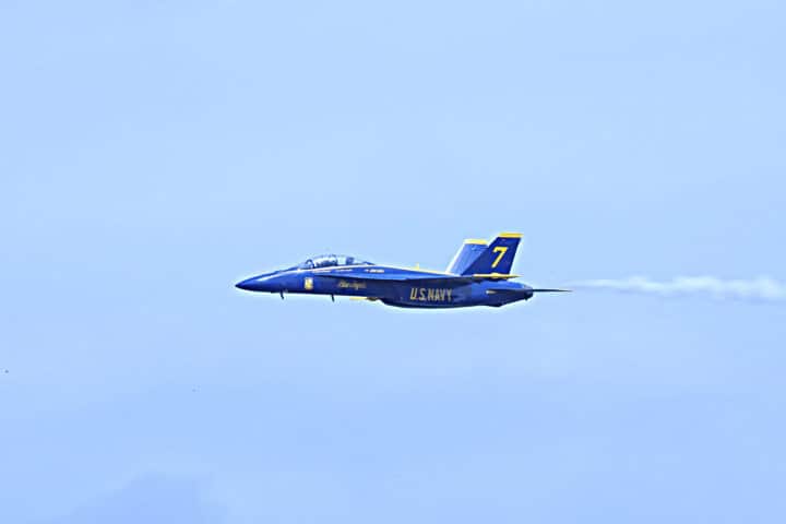 Single Blue Angels jet with smoke trailing behind it on a blue sky day