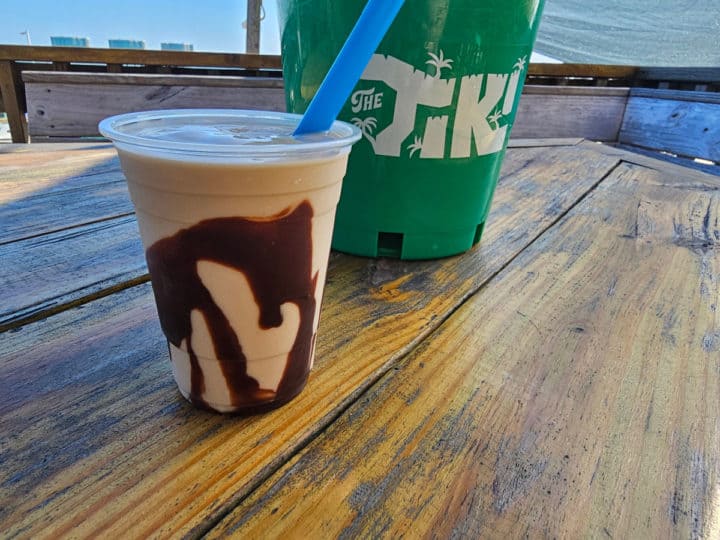 Bushwacker cocktail next to The Tiki green bucket on a table outside