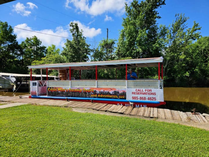 Cajun Man's Swamp Tours and Adventures sign on a red and white boat with a person onboard