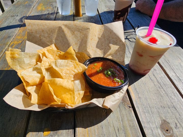 chips in salsa in a basket next to a frozen drink on a wooden table
