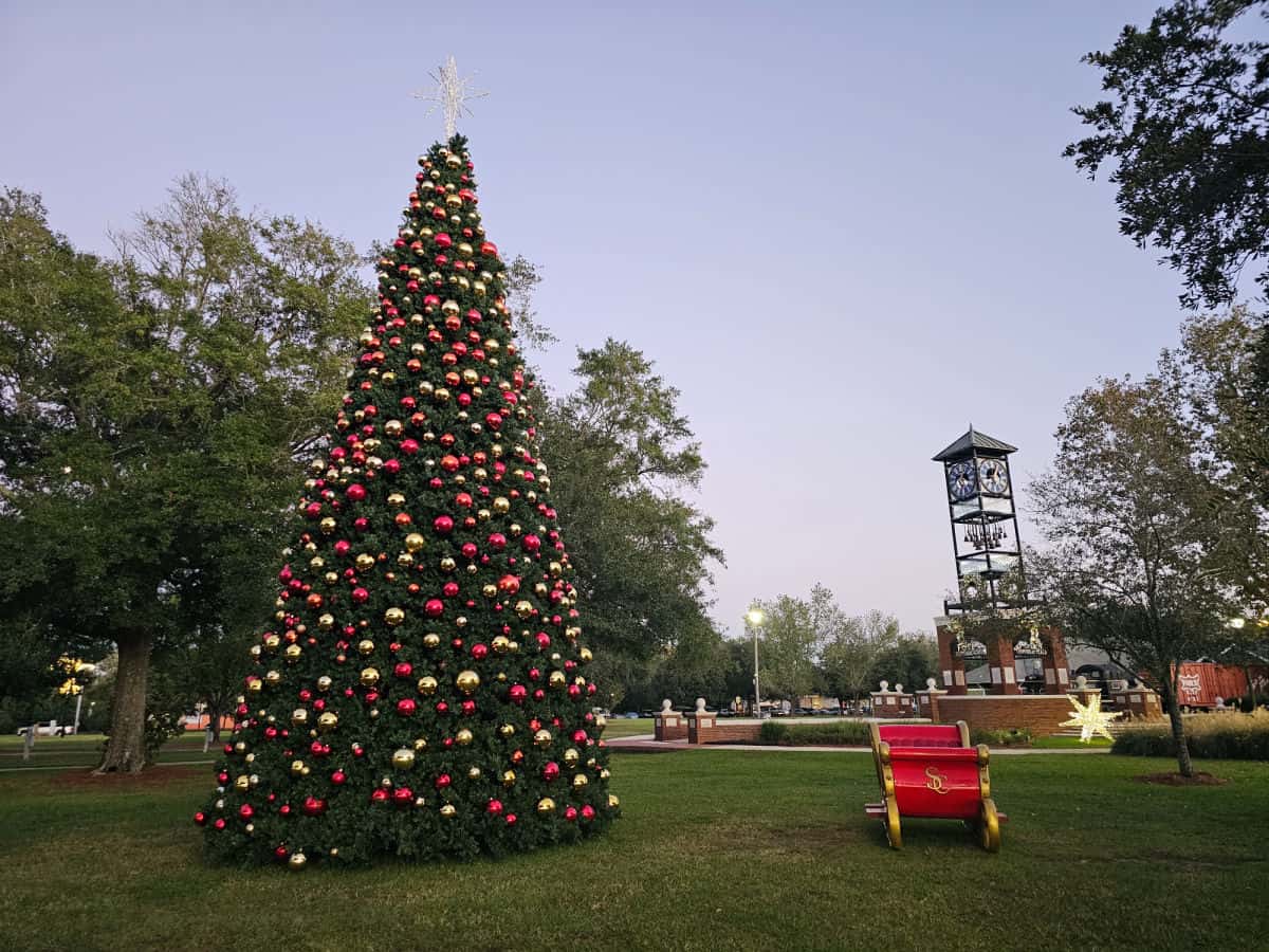 Christmas treee with gold and red balls next to a red and gold sleigh, Foley clock tower and trees in the background