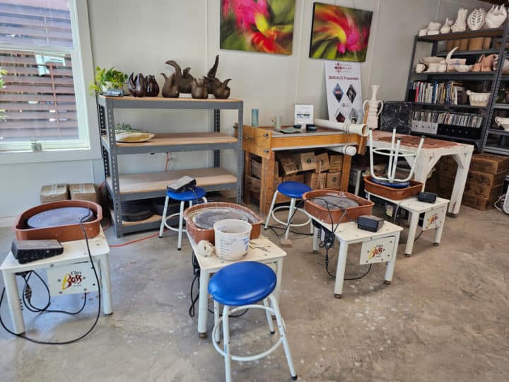 clay studio with multiple pottery wheels, pottery on shelves, and art on the wall