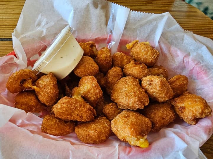 Corn fritters in a paper lined basket with a plastic container of ranch dressing 