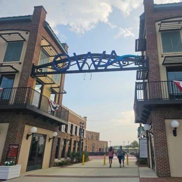 Blue OWA sign over a walkway between buildings with two people walking.