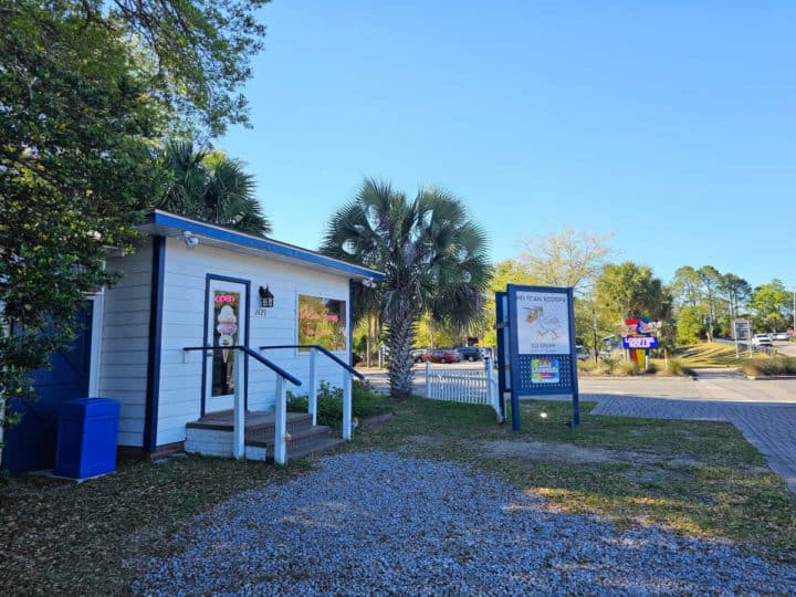 White building with blue trim with stairs at the front next to a white and blue sign for Pelican scoops ice cream 