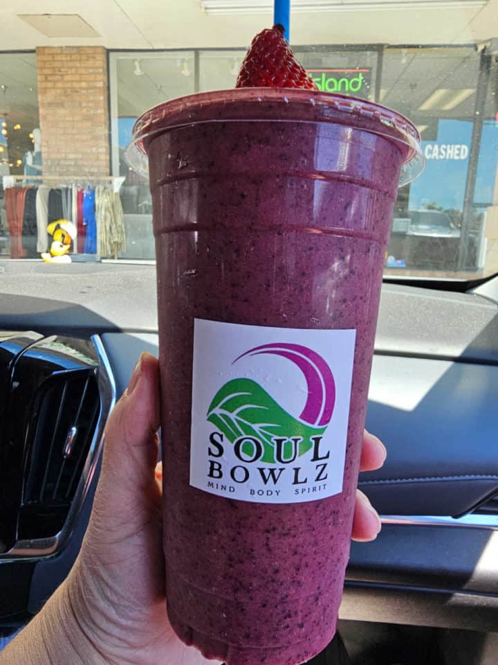Purple smoothie in a plastic cup with Soul Bowlz sticker and a strawberry on a straw