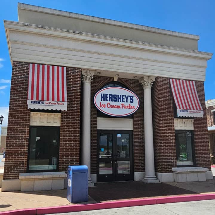 Hershey's Ice Cream Parlor sign over glass doors, with red and white awnings over two windows next to the door. 