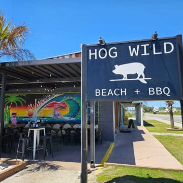 Hog Wild Beach + BBQ sign near a colorful mural with a surfing pig and palm trees