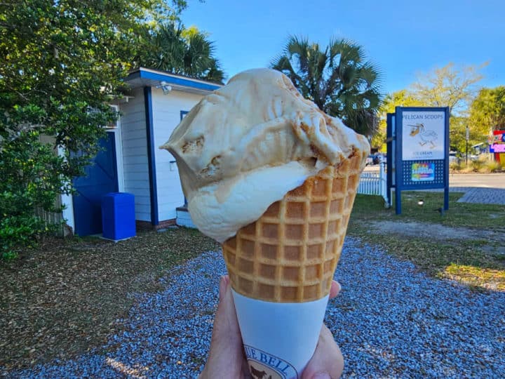 Hand holding an ice cream cone in front of the Pelican Scoops Ice Cream Sign. 