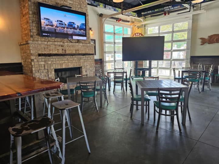 Indoor seating with tables and chairs, a fireplace with tv above it, and a tv on a stand near retractable garage doors