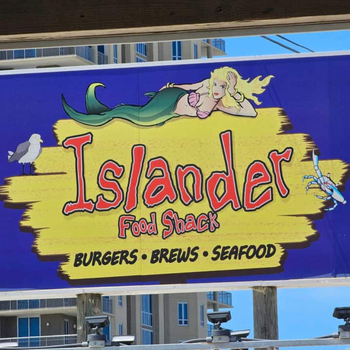 Islander Food Shack sign in yellow and black with a mermaid, seagull, and crab on it. 