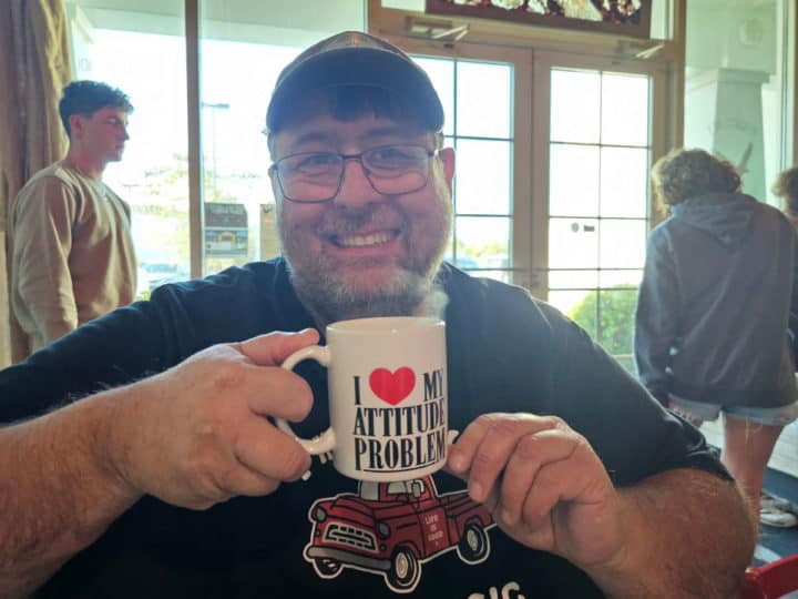 john holding a coffee mug with I heart my attitude problem with windows in the background