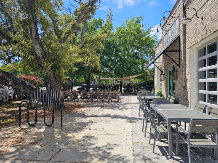 outdoor seating with tables and chairs along with Adirondack chairs on a large patio with trees