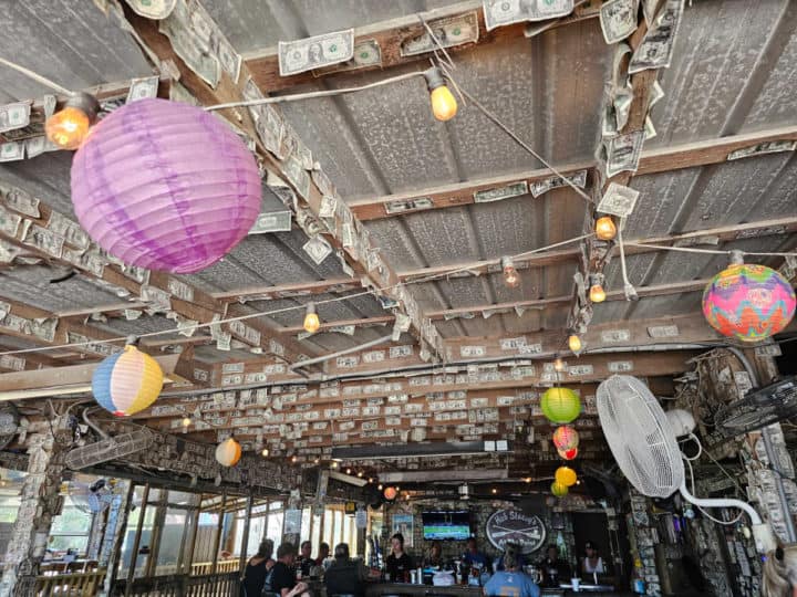 outdoor seating with dollar bills stapled to the ceiling and rafters, Hub Stacey's at the Point sign behind a large bar with people sitting around it. 