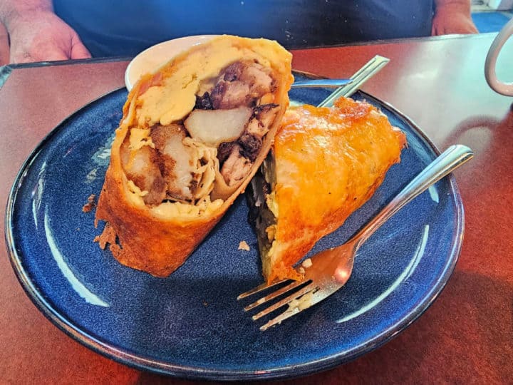 pork belly burrito with cheese on the outside on a blue plate with a fork. 