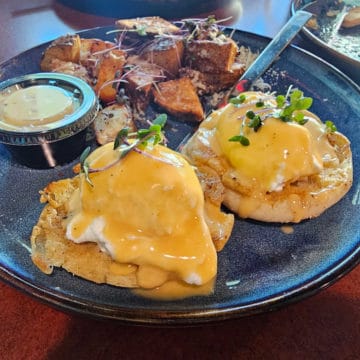 Eggs benedict next to truffle potatoes on a blue late with a knife
