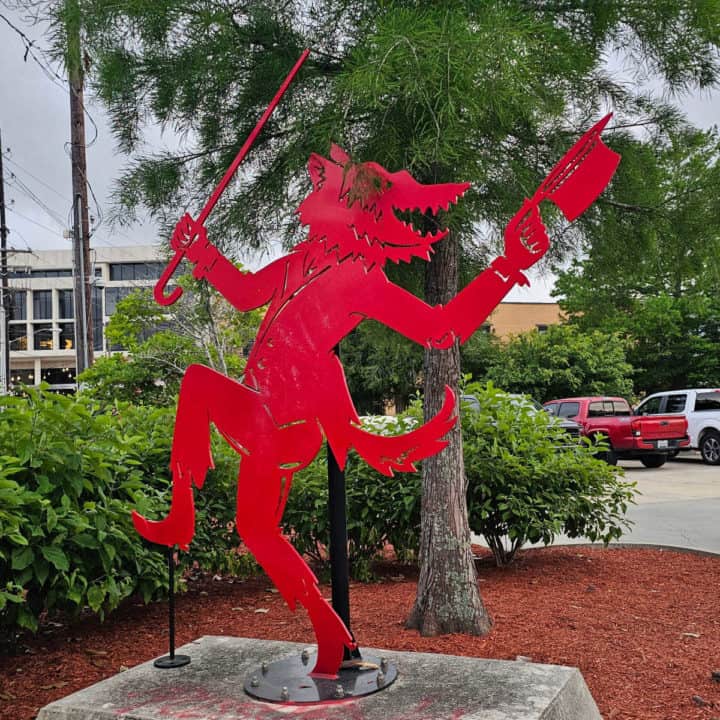 Red Rougarou Statue with trees around it. 