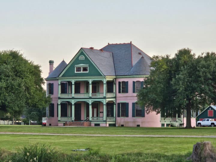 Pink and green two story plantation house with grassy lawn