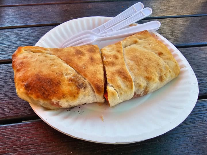 Stromboli on a paper plate with plastic silverware