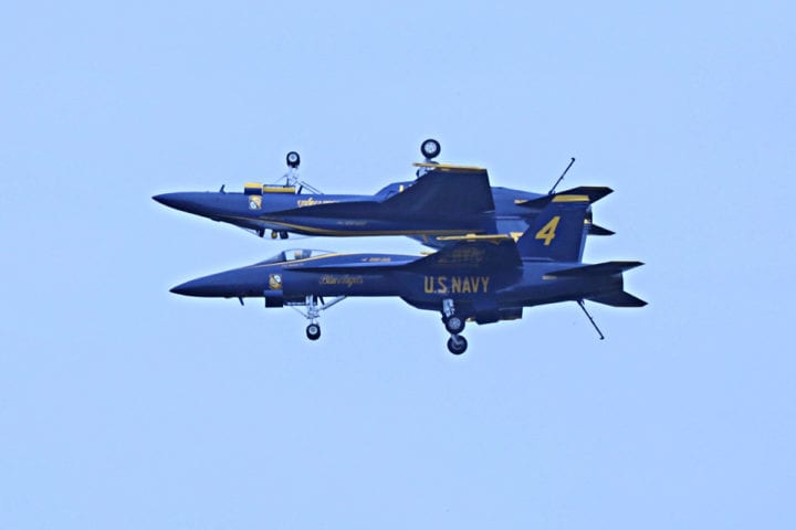 Two Blue Angels planes flying in sync with one upside down over the other. 