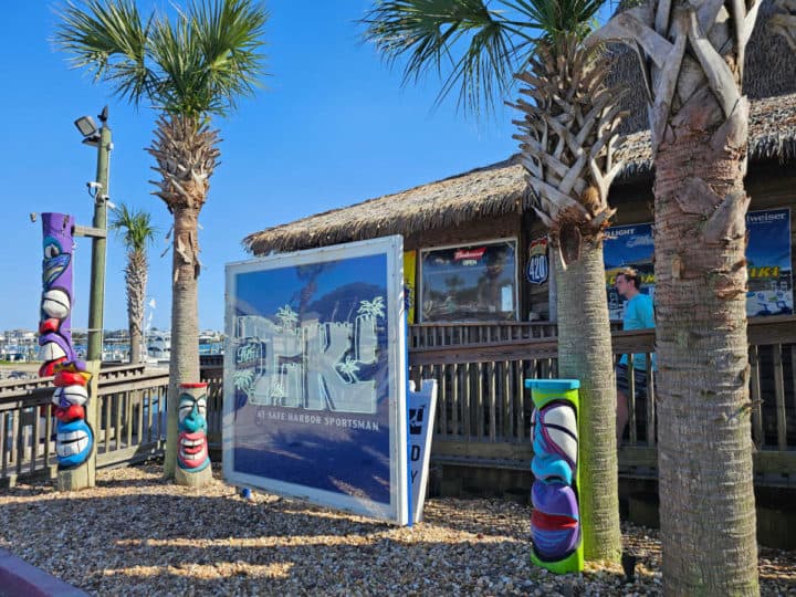 The Tiki at Sportsman Harbor Marina sign next to tiki statues and palm trees