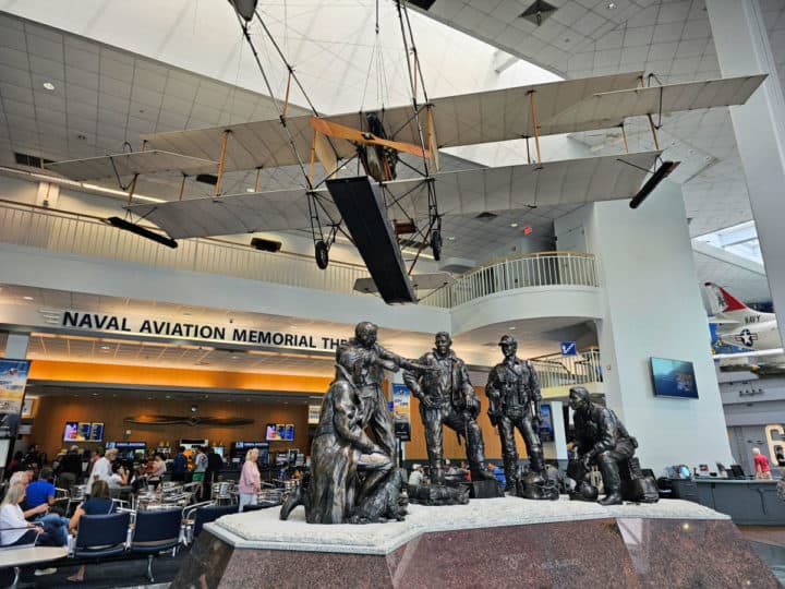 Airmen statue with Naval Aviation Memorial Theater behind it with people sitting at tables 