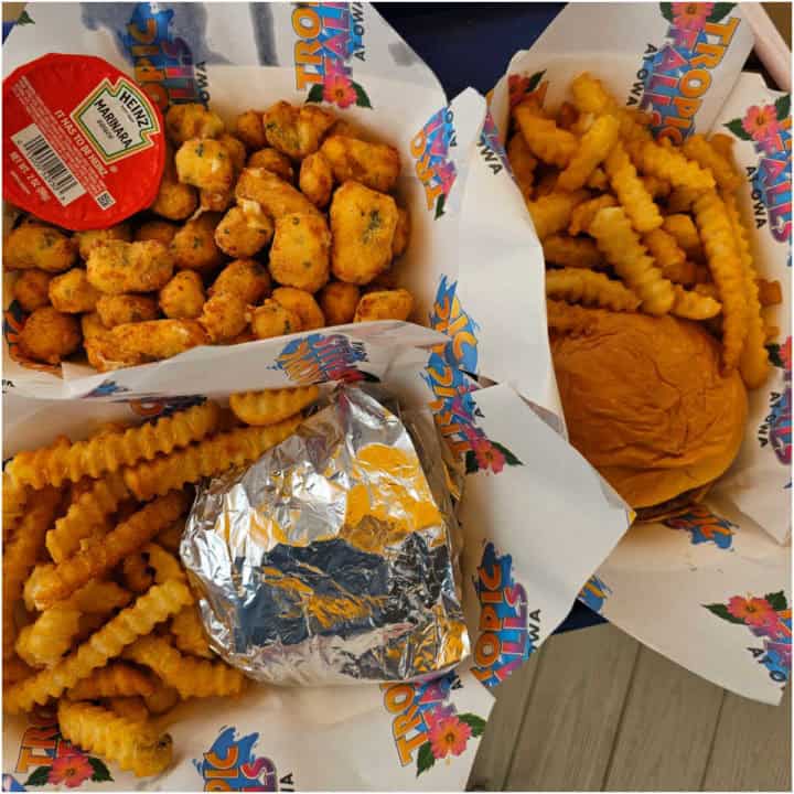 Three paper baskets with a burger and fries, cheese curds, and foil wrapped cheeseburger, with Tropic Falls at OWA paper under them. 