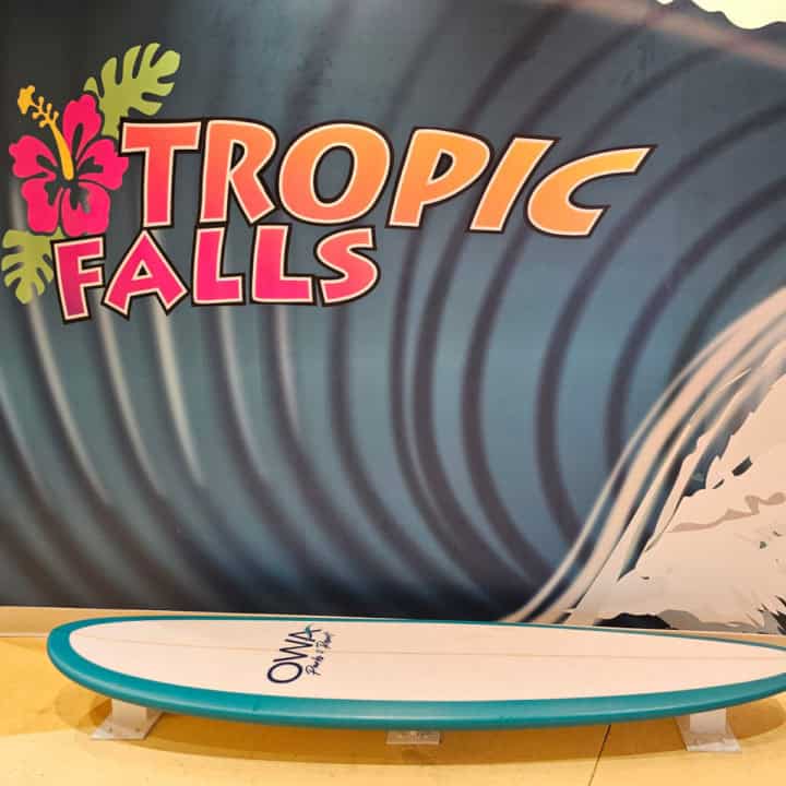 Tropic Falls logo on a painted wave on the wall above a surfboard with OWA printed on it. 