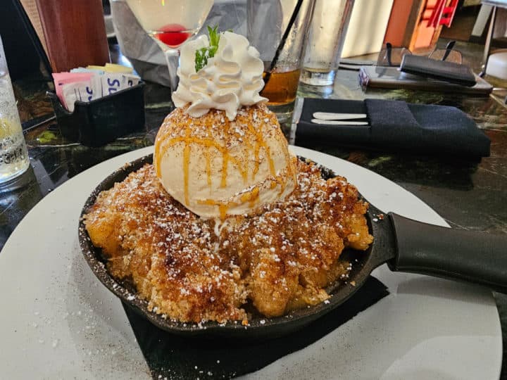 Apple crisp in a cast iron skillet with ice cream, caramel, and whipped cream