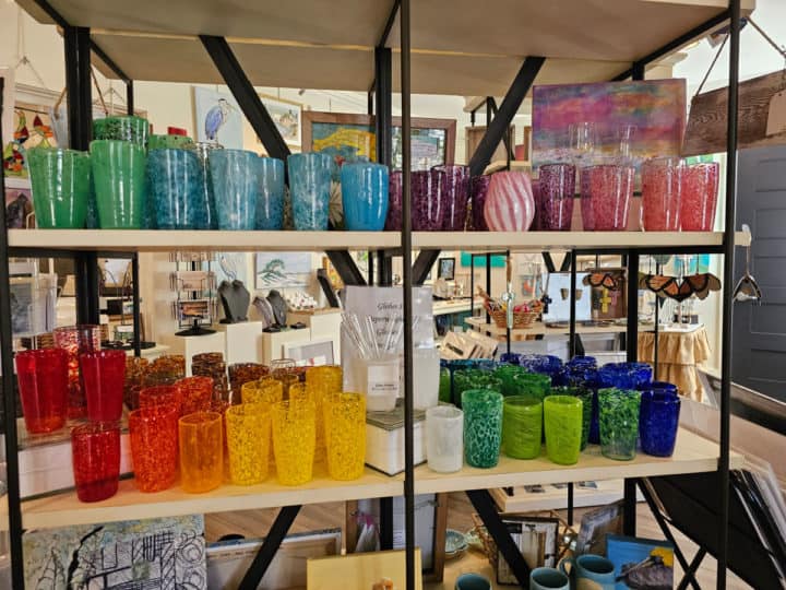 blown glass glasses on display in a rainbow order on two shelves