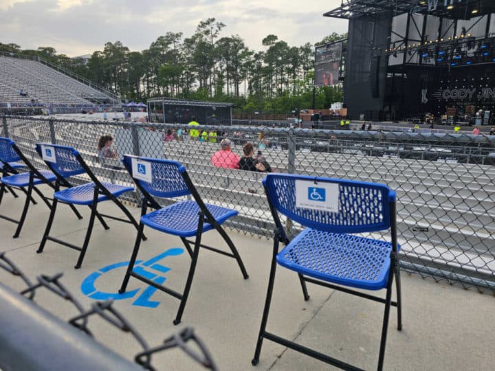 blue folding chairs with accessible seating tags next to a metal fence with the Wharf Amphitheater in the background. 