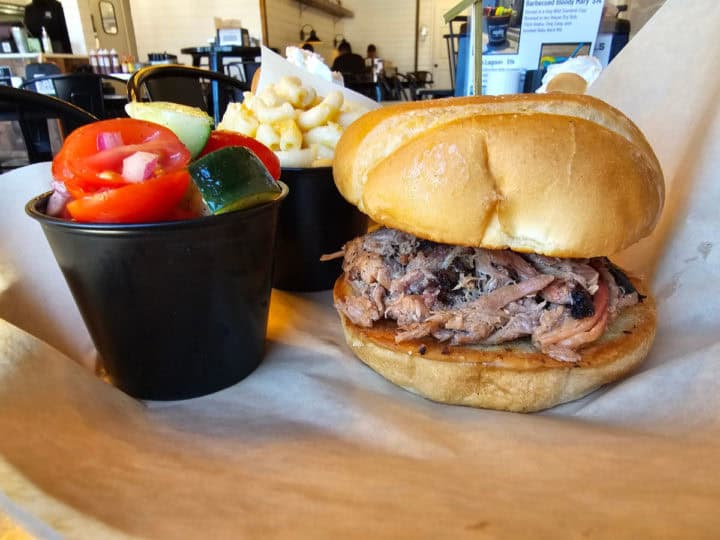 Brisket sandwich next to a container of mac and cheese and tomato cucumber salad