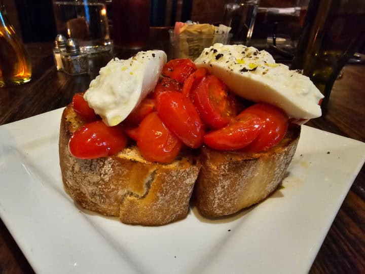 large bread slices with tomatoes, and burrata mozzarella on top with seasoning on a white plate